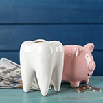 A pink piggy bank and a fake tooth next to hundred-dollar bills