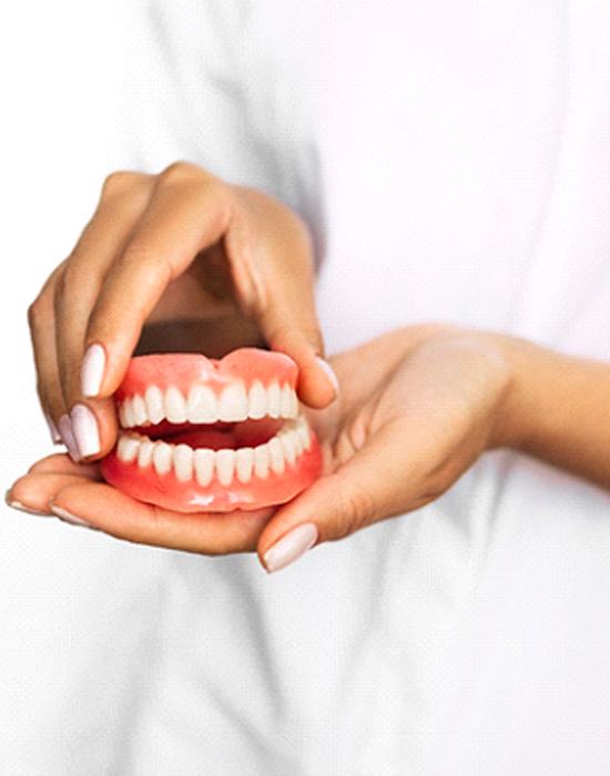 Closeup of dentist holding dentures in Fort Worth