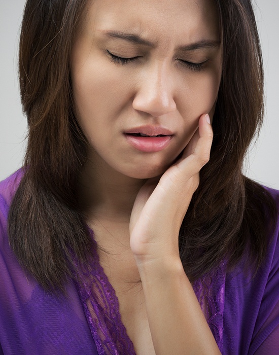 Woman in need of emergency dentistry holding cheek in pain