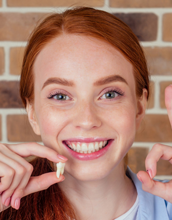Smiling woman making “ok” sign with one hand while holding extracted tooth in the other