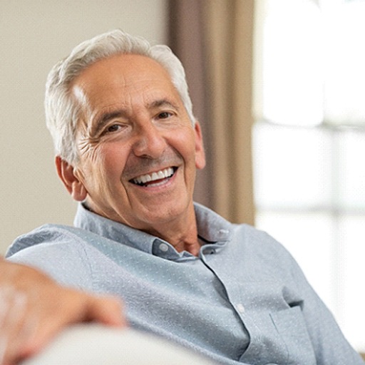 Senior man on couch smiling with implant dentures in Fort Worth, TX