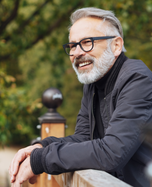 Older man leaning against wooden railing outdoors