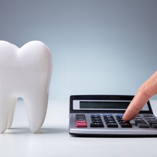 hand typing on calculator next to model of tooth