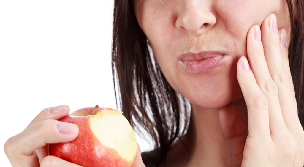 A woman with a sore jaw eating an apple