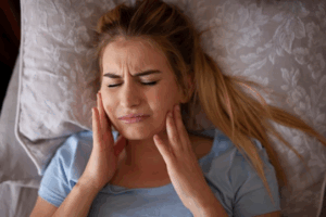 Woman lying in bed and rubbing her aching tooth